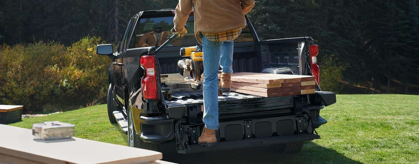 A man is shown stepping onto the liftgate of a black 2022 Chevy Silverado 1500 after visiting a Chevy dealer.