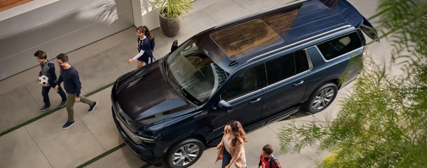 A dark grey 2023 Chevy Suburban is shown parked as people walk by.