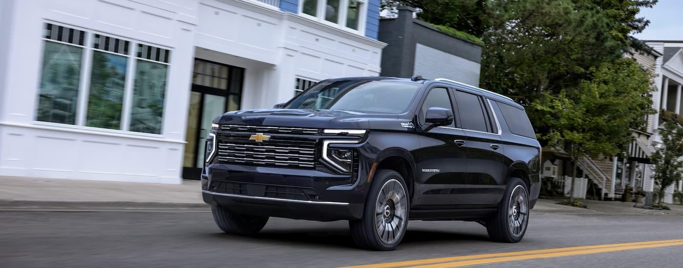 A black 2025 Chevy Suburban High Country is driving on a city street after leaving a Chevy dealer near Jonesville.