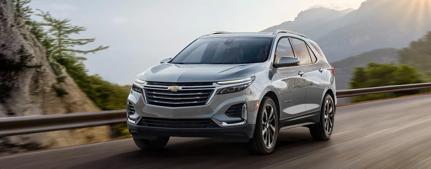 A silver 2024 Chevy Equinox is shown driving on a mountain road.