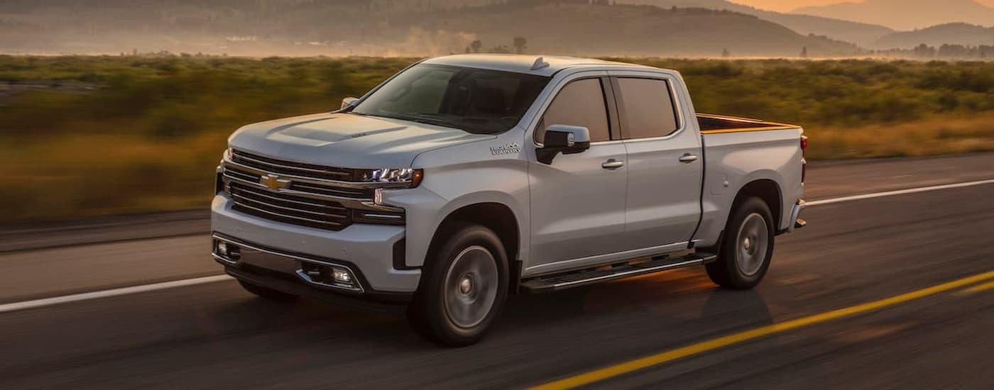 A white 2019 Chevy Silverado 1500 High Country is driving on an open road after viewing used trucks for sale.