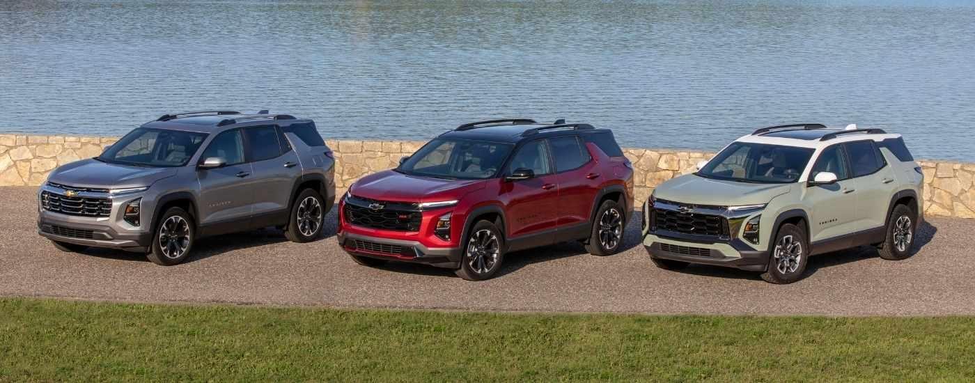 A grey, a red, and a tan 2025 Chevy Equinox are lined up in front of a river.
