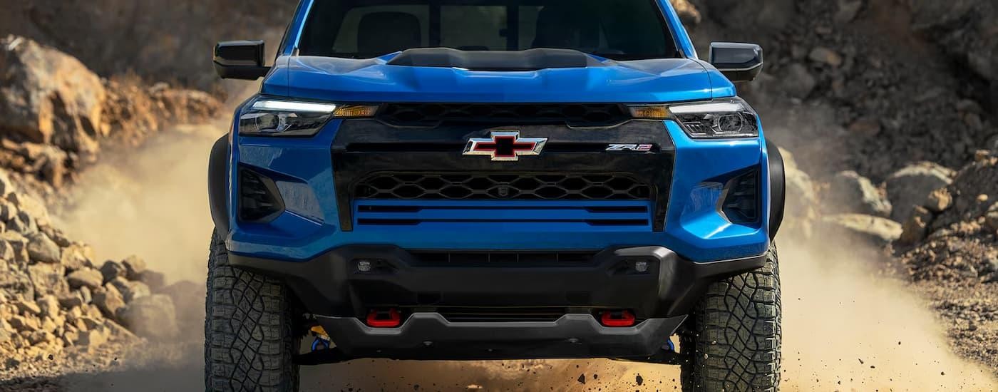 A blue 2024 Chevy Colorado ZR2 is driving on a dusty rocky road.