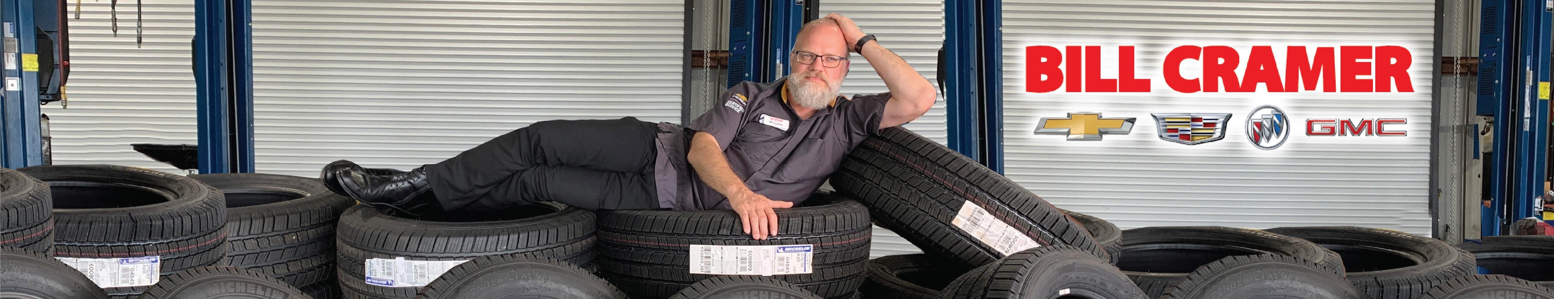 Tires at Cost with Bill Cramer | Technician laying on pile of Brand New Tires for SALE