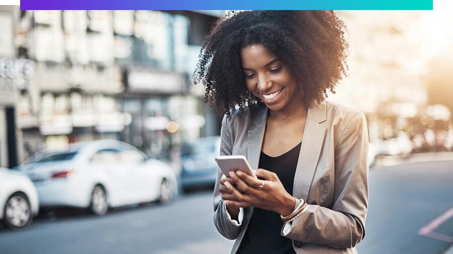 Smiling woman walking down a street while looking at her phone