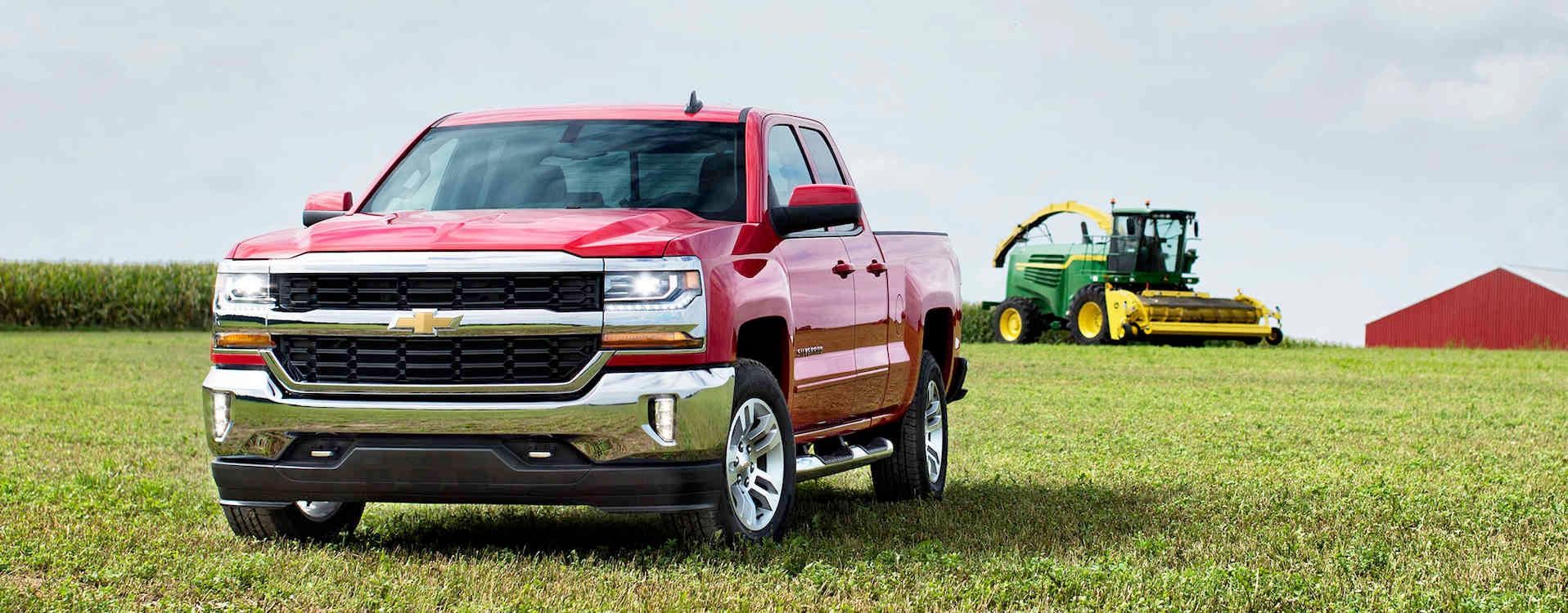 A red 2018 Chevy Silverado 1500 parked on grass near a large farm machine