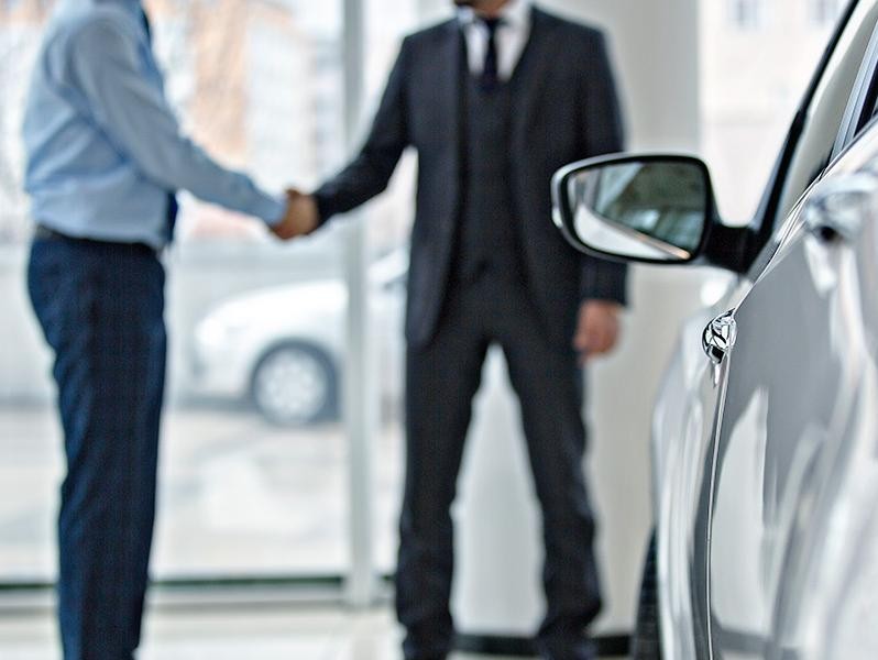 Two people shaking hands near a vehicle at dealership