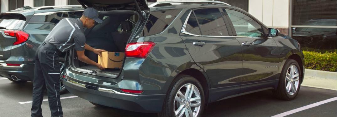 Amazon delivery man places a package into the rear cargo area of a 2018 Chevy Equinox
