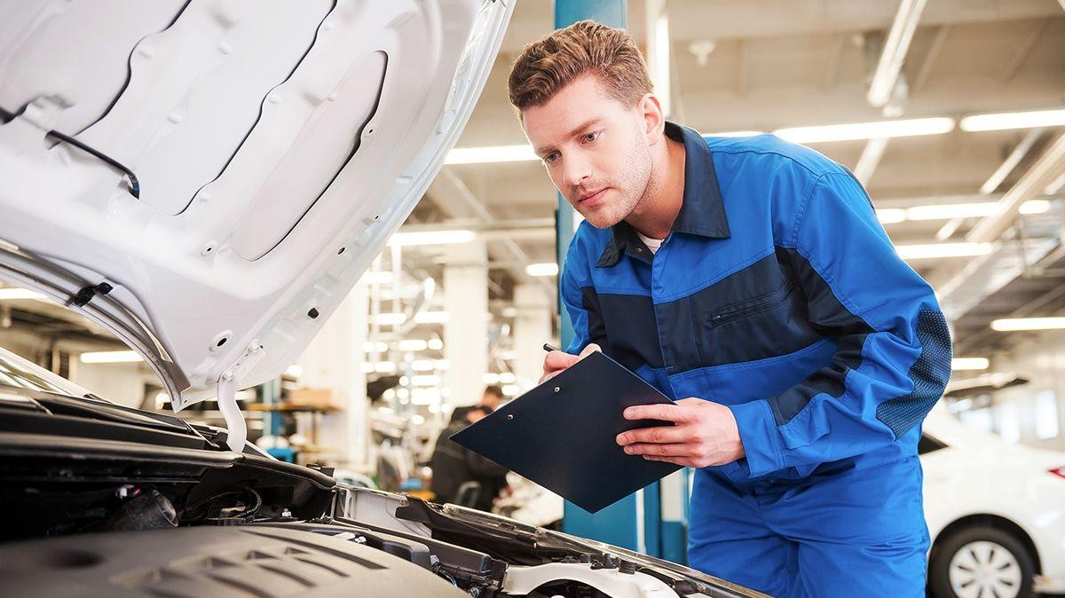 Mechanic holding clip-board servicing vehicle.