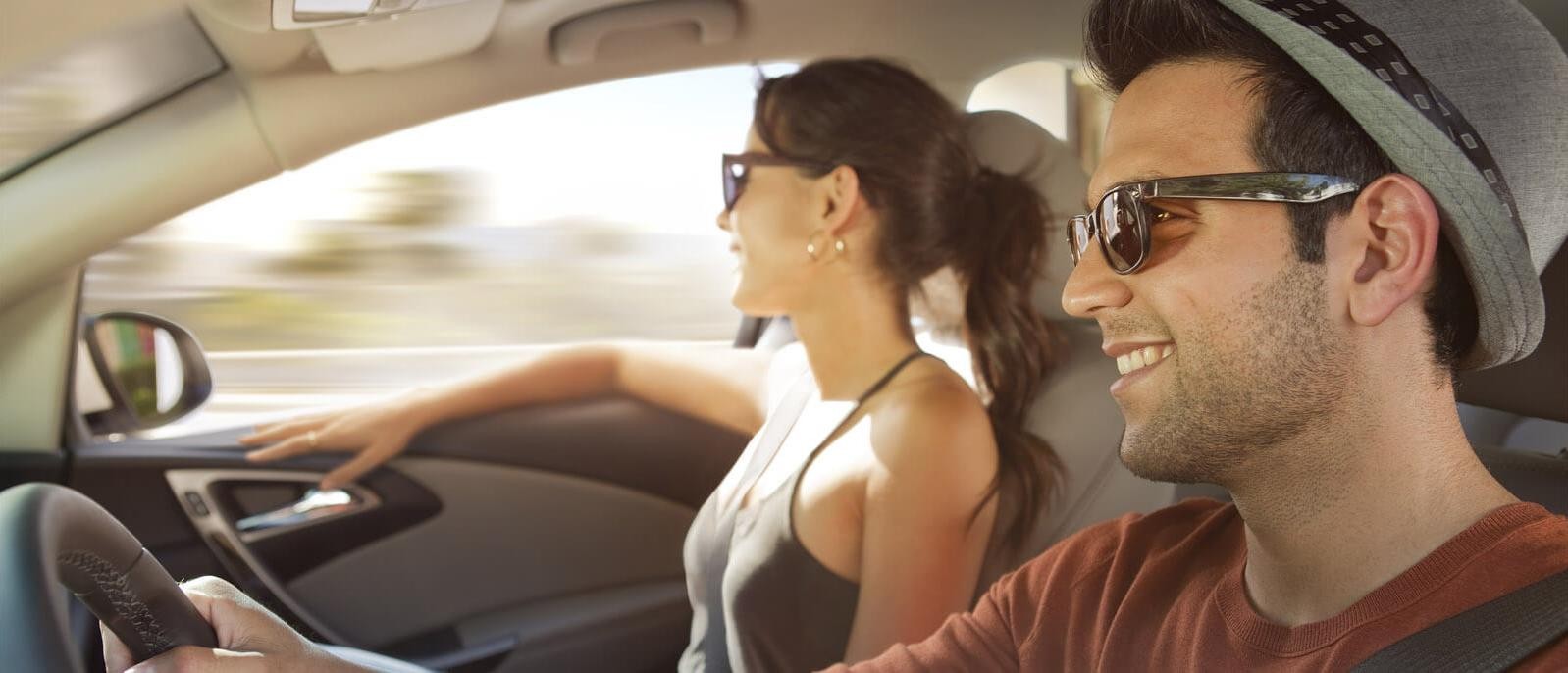 A young couple laughing and driving on a sunny day.