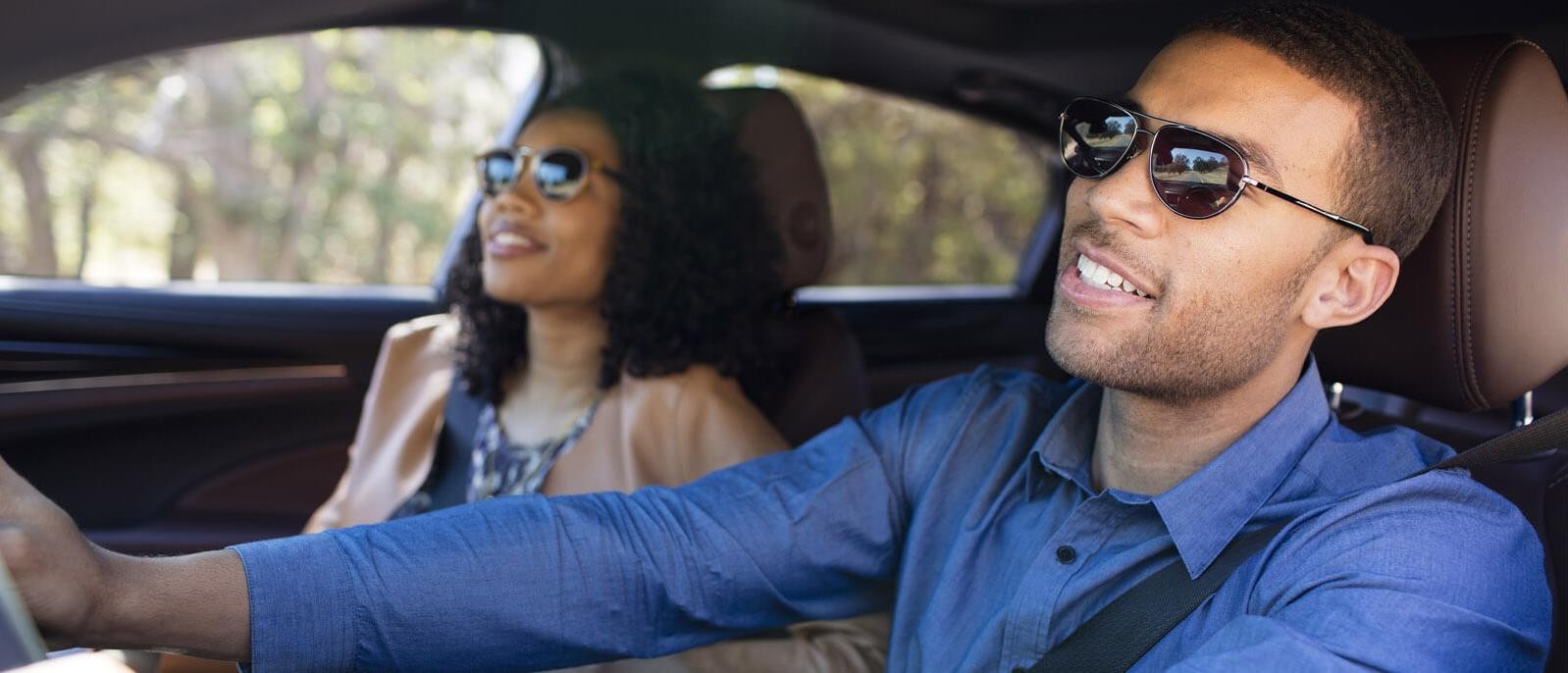 A cool couple leaning back and smiling while driving with sunglasses on.