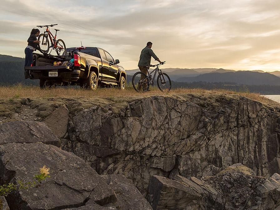 A couple unloading bikes from their 2018 Colorado on a bluff overlooking a lake.